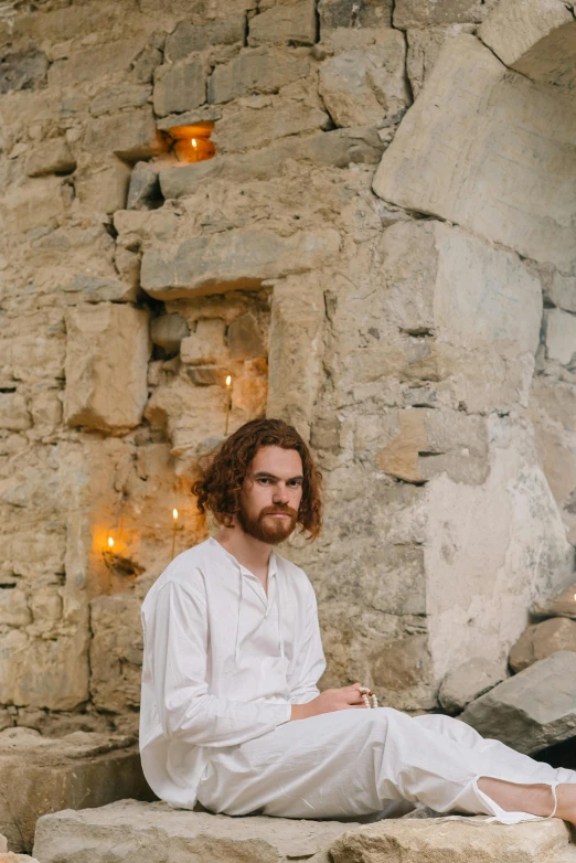 a man in white sits on a rock and lights candles