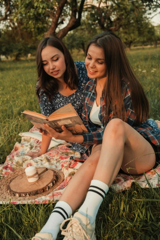 two girls are reading outside in the grass