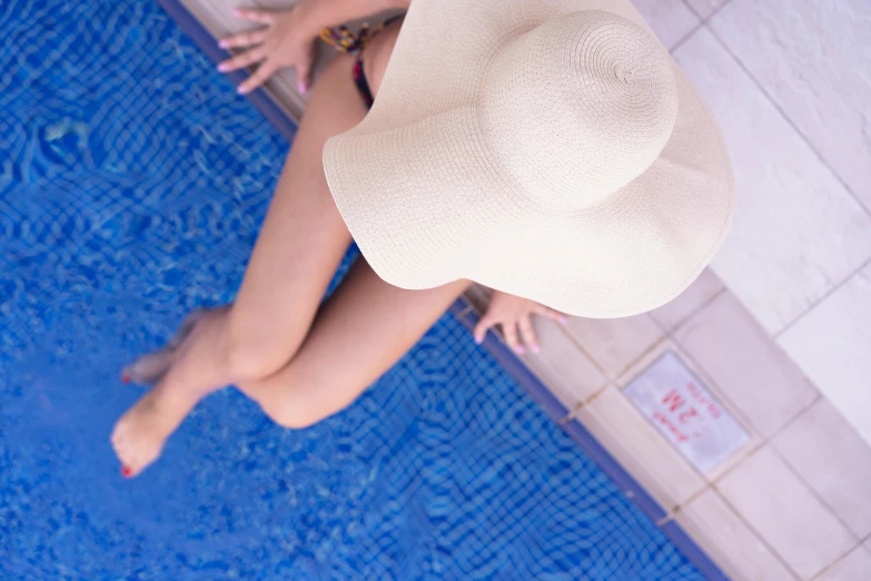 a young woman's legs and white hat leaning on a pool edge