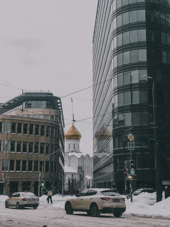 several cars drive on a snowy street and building in the background