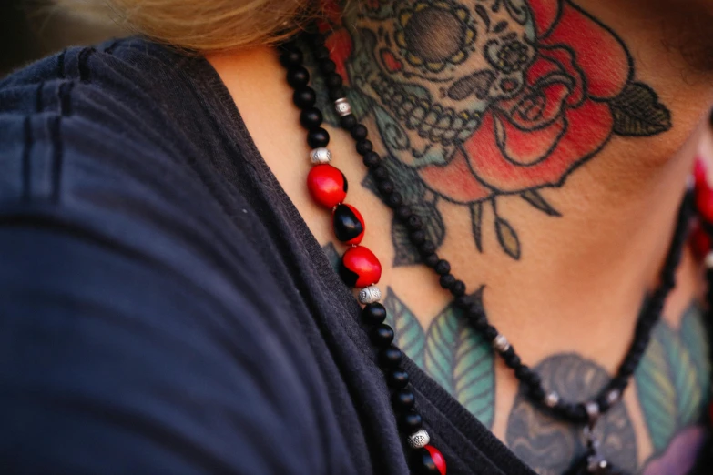 a person with tattoos on her chest and a long black necklace with red beads