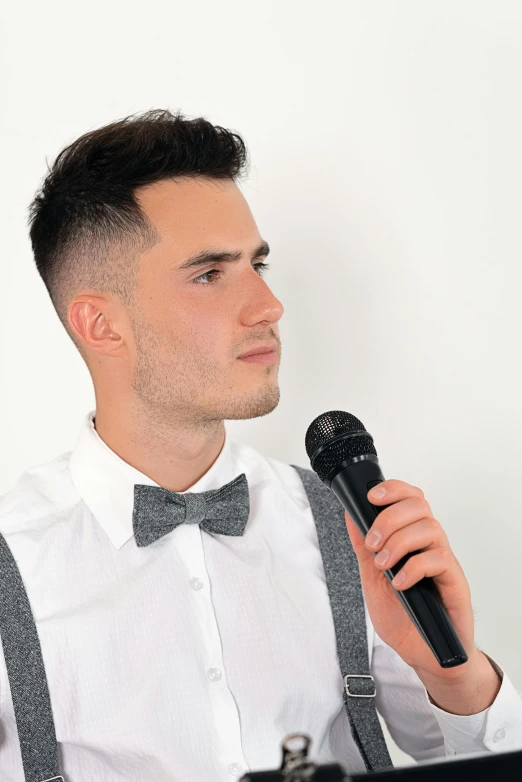 a man wearing suspenders and a bow tie singing into a microphone