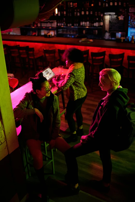 three people sitting at a bar with neon lights