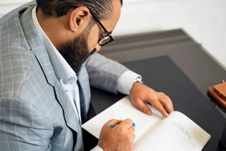 a man in a suit and glasses sitting at a desk with a book