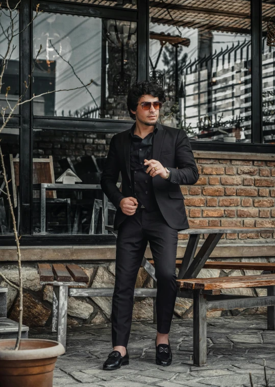 man in black suit leaning on bench wearing sunglasses