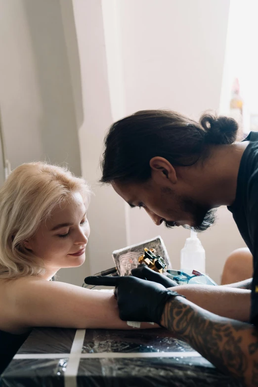 a young man helping a woman with her tattoo