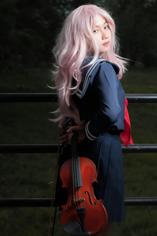 a woman with long hair playing violin by a fence