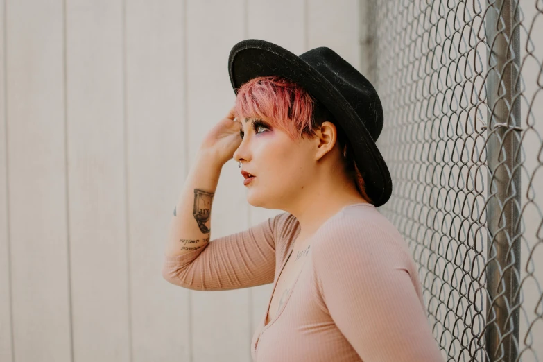 young woman with dyed hair and black hat poses by the fence