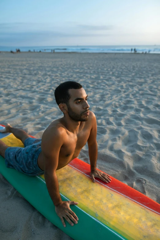 a shirtless man laying on his surfboard at the beach