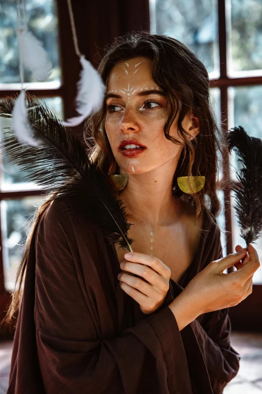 a woman is holding feathers with the window behind her