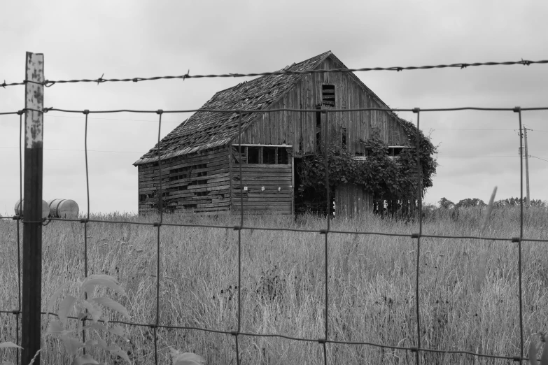 an old barn sits behind a barbed wire fence