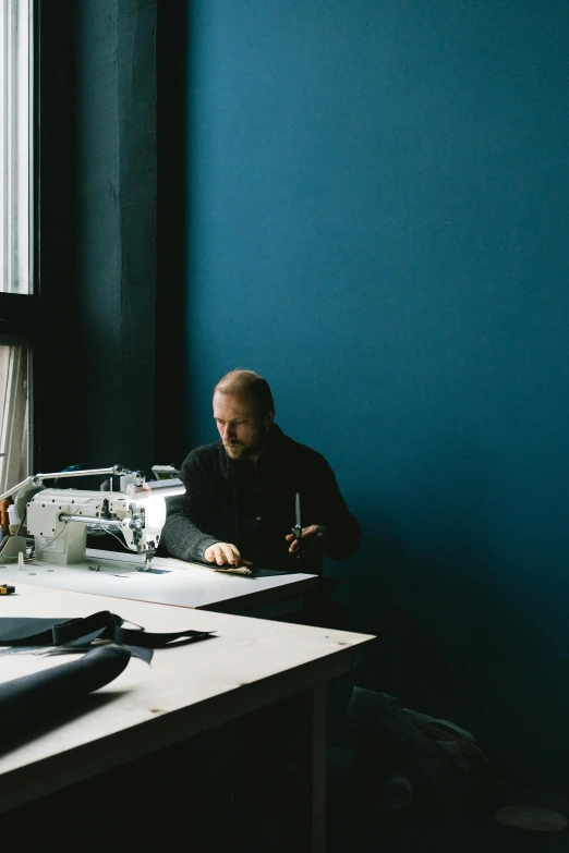 a person sitting at a table sewing on a sewing machine