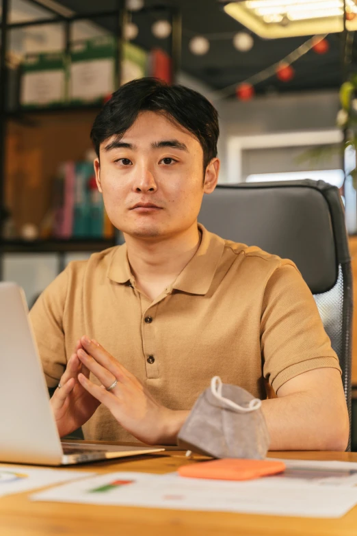 an asian man sitting in front of a laptop computer