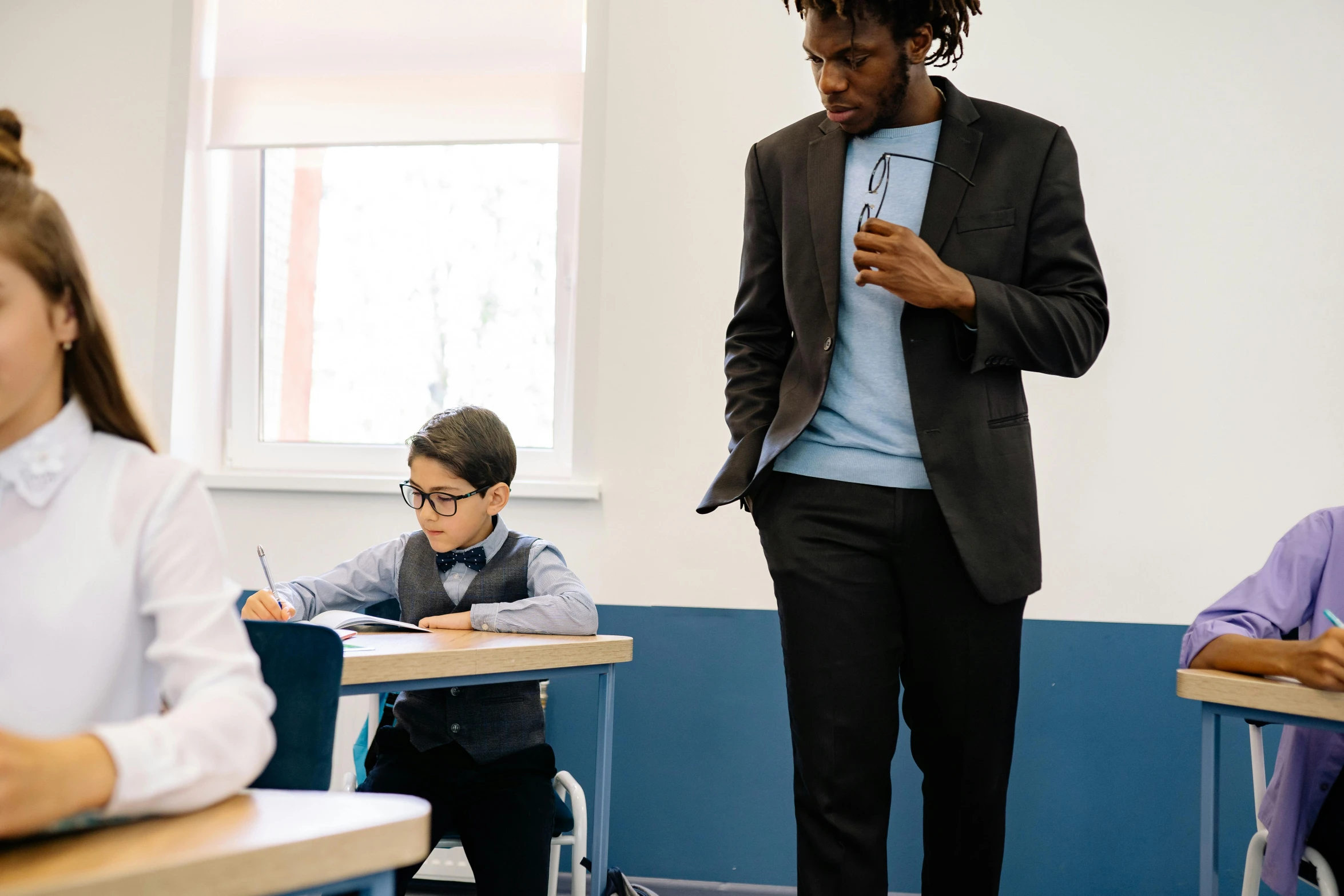 there is a person standing in the classroom and he has his hand over his tie