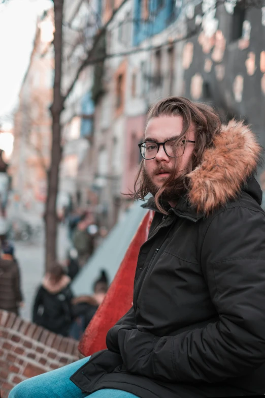 a man with long hair and glasses sitting on a bench