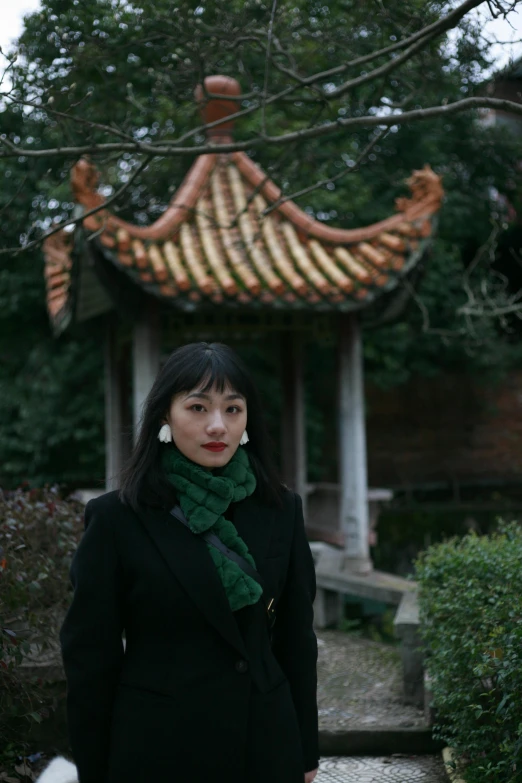 a women in a coat and scarf standing near a pagoda