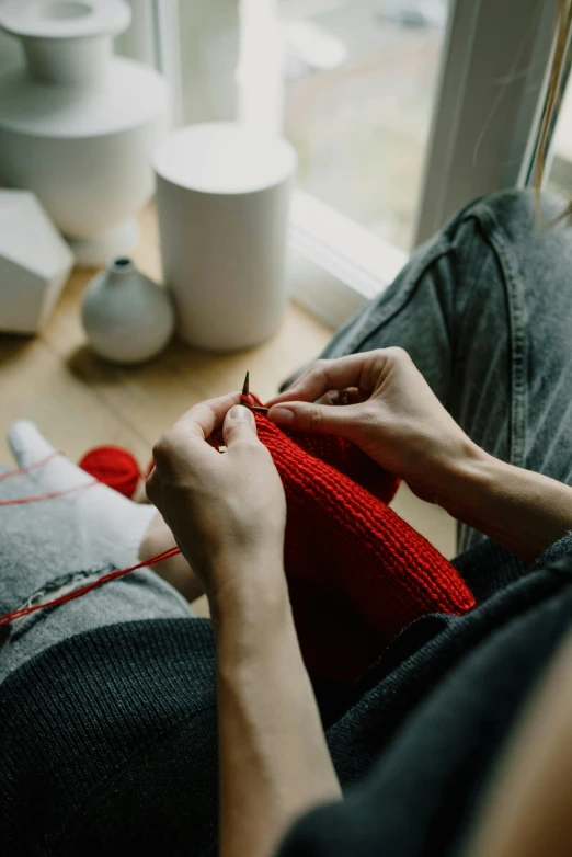 a woman knitting at the window with red yarn