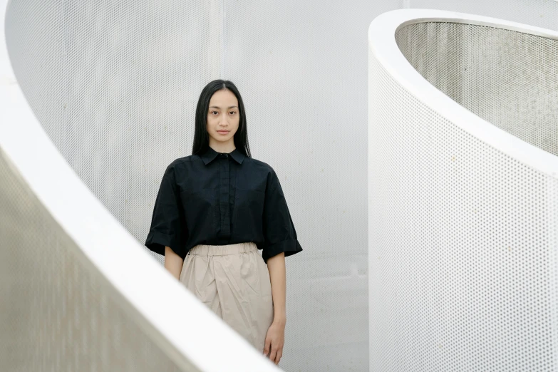 an asian woman in black shirt standing by some white wall