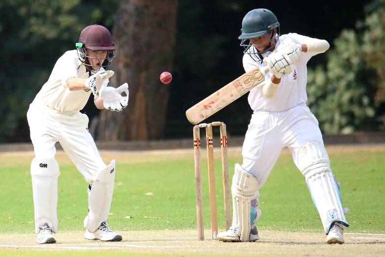 two young men playing cricket and one swinging a bat at the ball