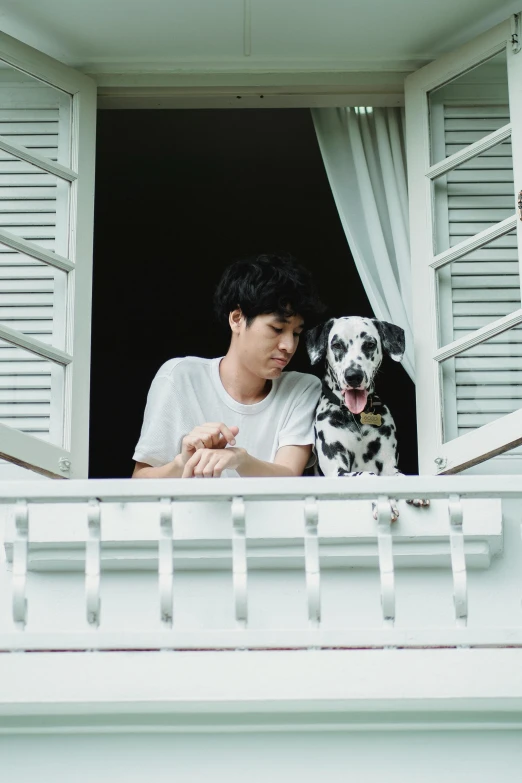 a man standing at a window with a black and white dog looking out the window