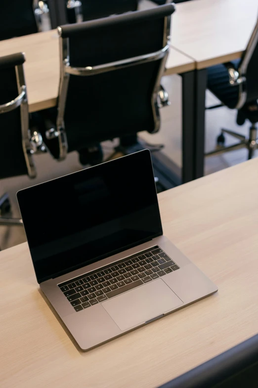 a laptop is on a wooden table in a room with several chairs