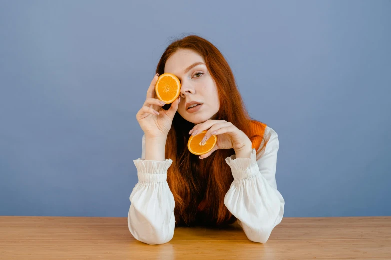a beautiful woman holding two orange slices with her fingers