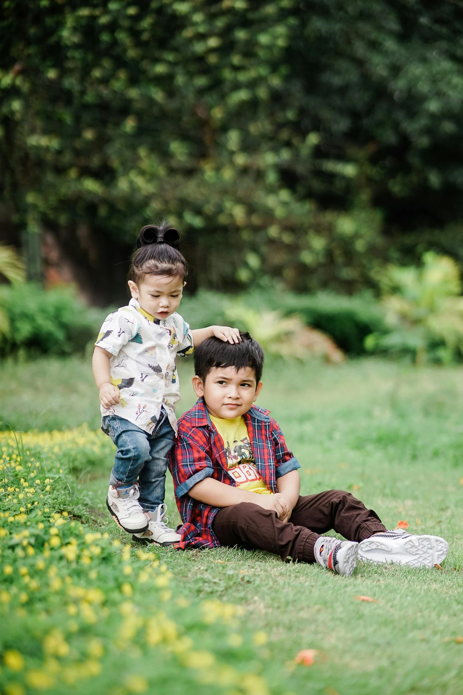 a boy sitting next to another small boy in the grass