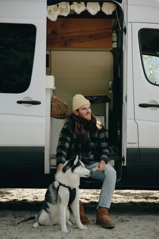 a man sitting on a van next to his dog