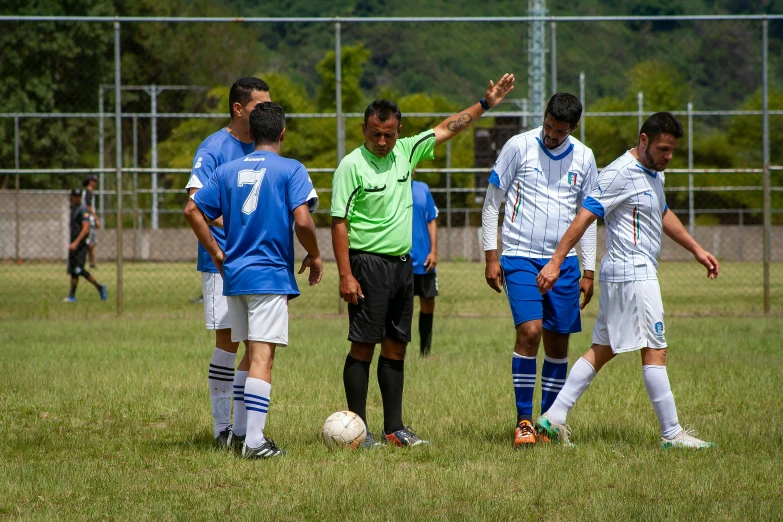 two teams of soccer players are in a field with a referee