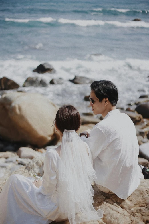 two people sit on a rocky shore near the ocean