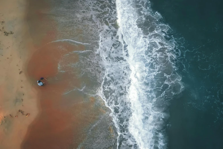 an aerial view of a beach with waves coming towards a white cloud