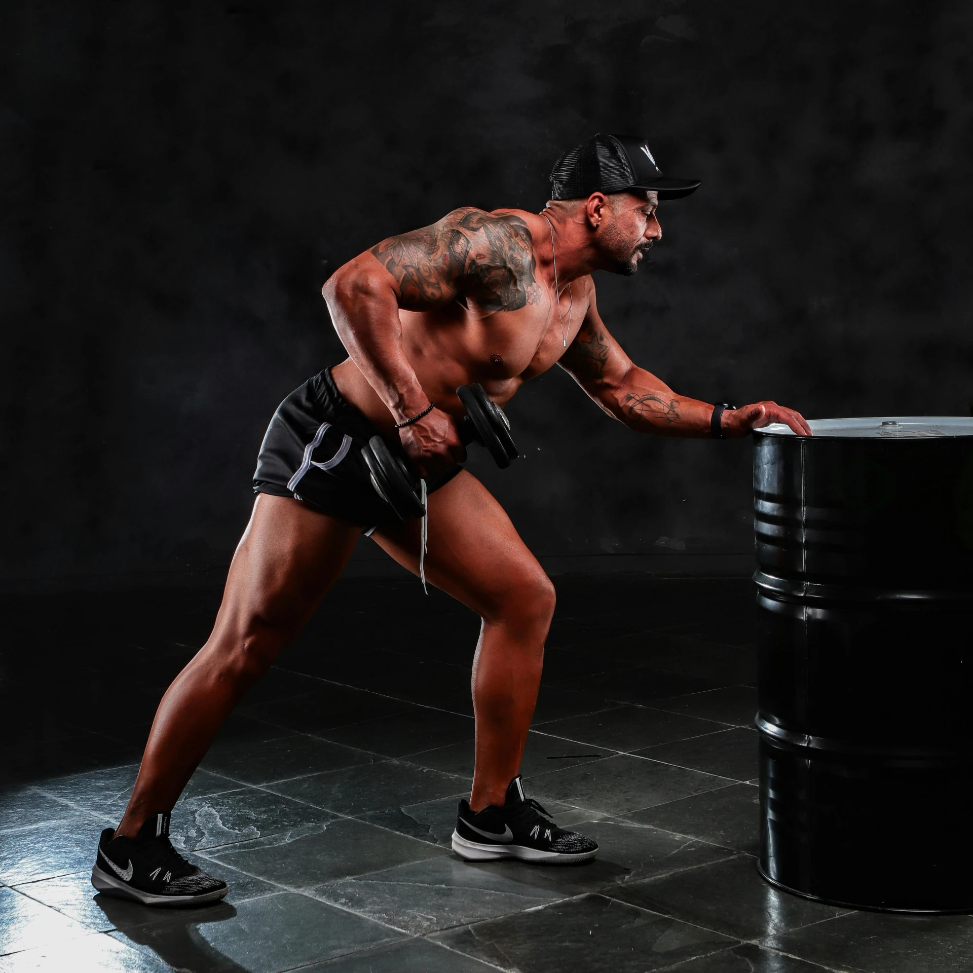 man in shorts and black hat, leaning on a black barrel