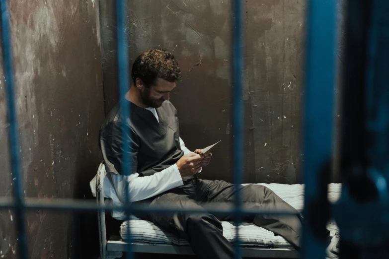 a man sits on a prison cell looking at a smart phone