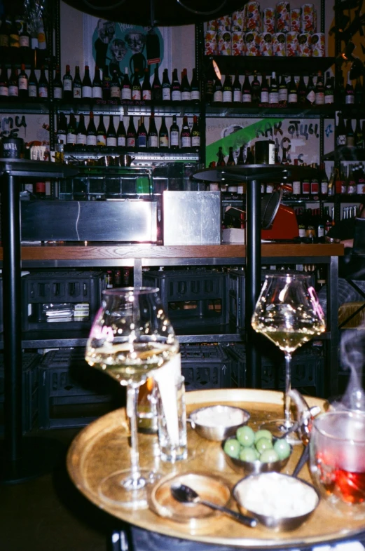 two wine glasses sitting on a small round table with utensils in front of bottles