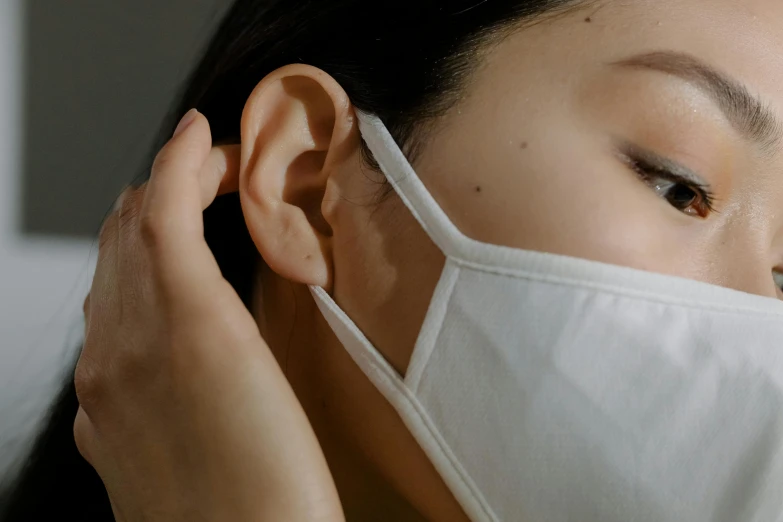 a woman wearing a white mask puts on her ear