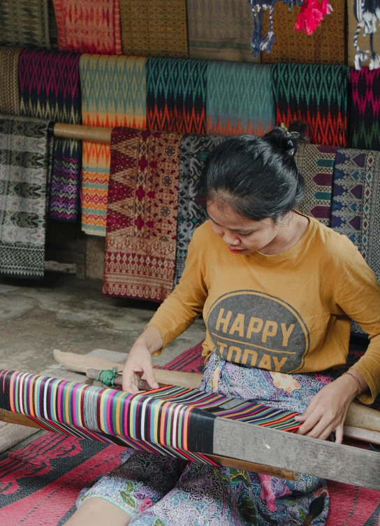 a lady weaving some fabric on top of a wooden mat