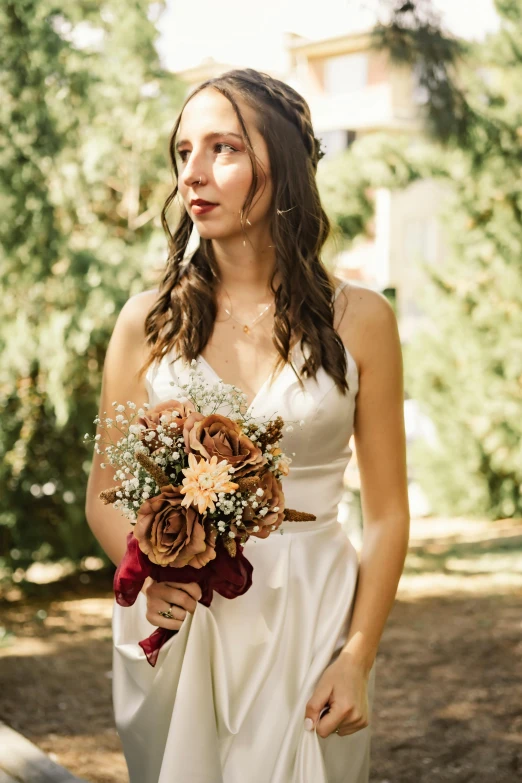 a woman holding a bridal bouquet standing in front of trees