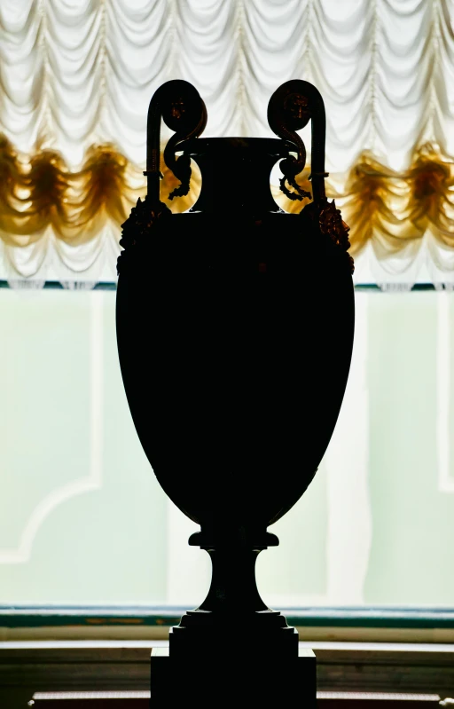 a large vase sits on a pedestal beside a window