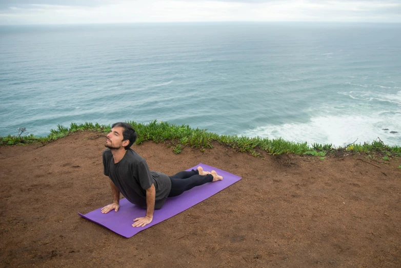 a man is stretching on the beach on a purple mat
