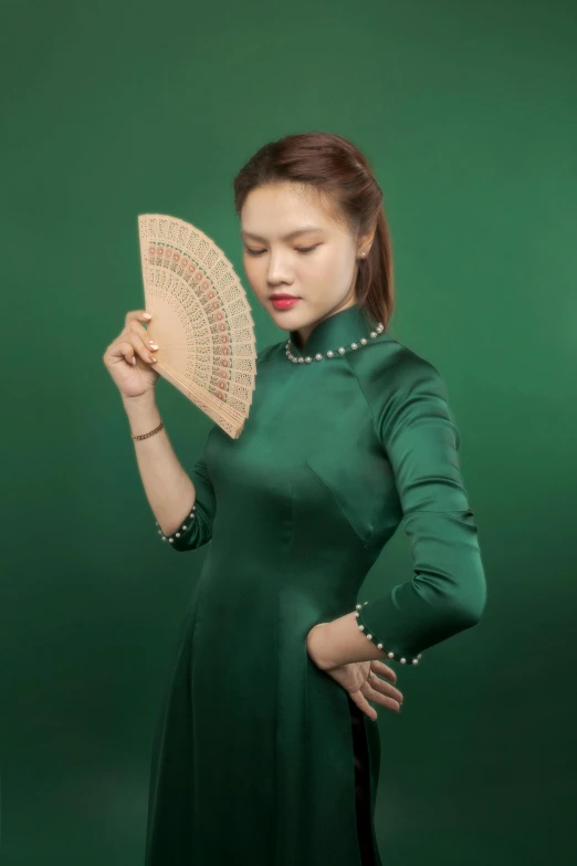 a woman wearing green poses with an ornate fan