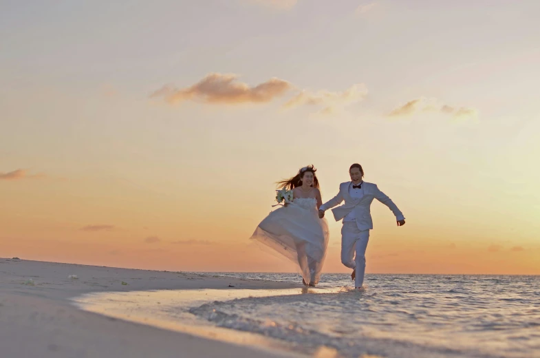 bride and groom running in the surf holding hands