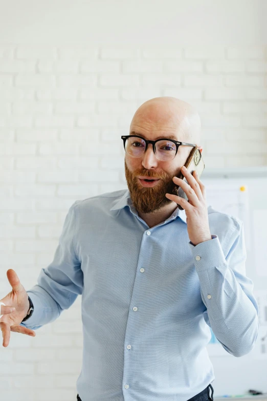 a bald man talking on the phone while wearing a blue shirt