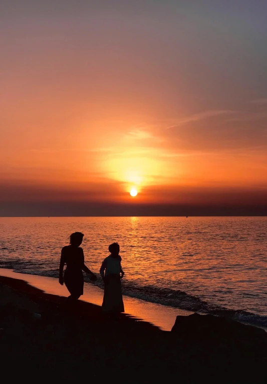 a couple walks along a beach at sunset