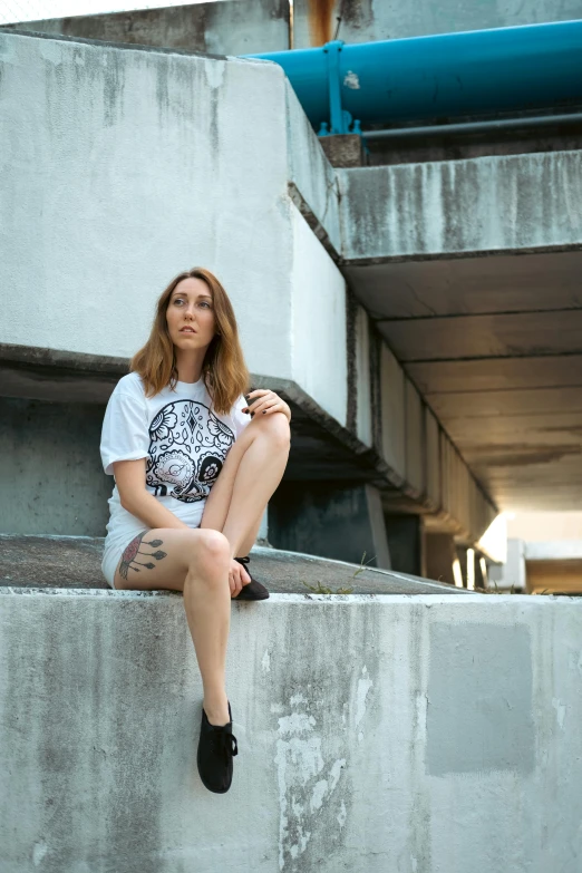 a woman sits on concrete ledge next to a pipe