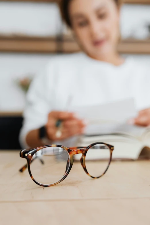 woman reading book while looking through her glasses