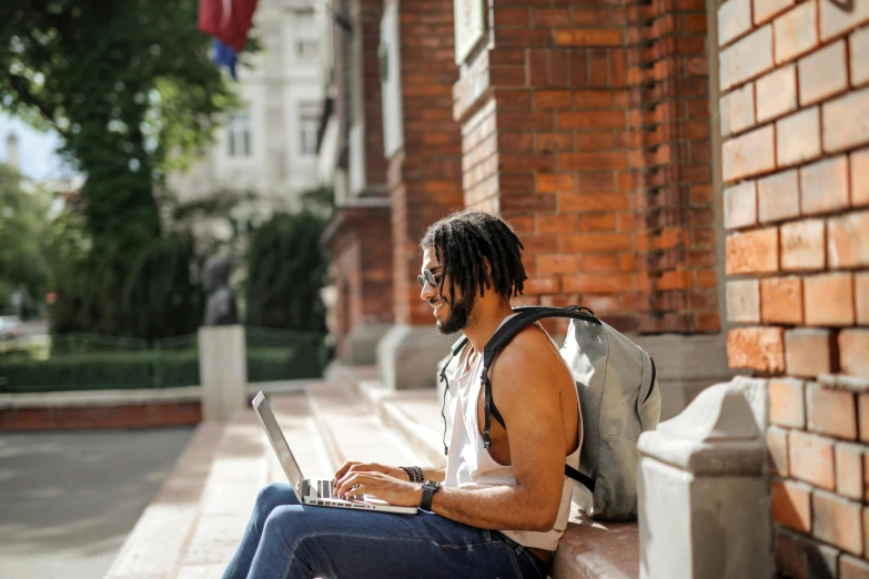 a man in a backpack sits with a laptop on a ledge