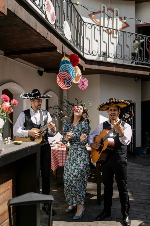 two guys and a woman wearing mexican attire are standing in front of an outdoor bar with string lights