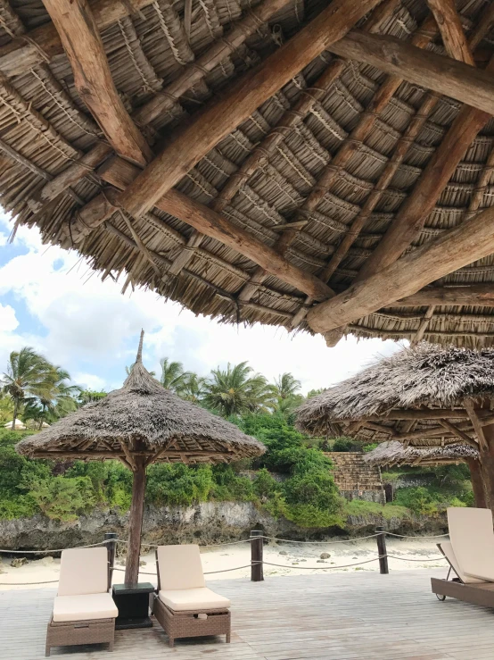 a couple of lounge chairs under a thatched roof