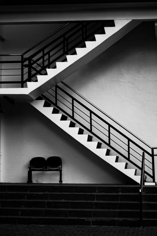 two empty chairs under a stairwell of a white building