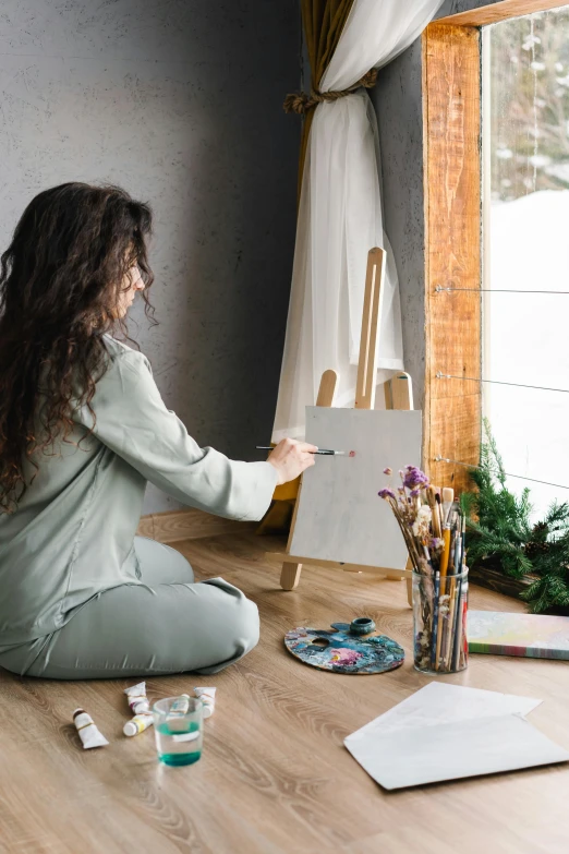 a woman is sitting on the floor in front of an easel